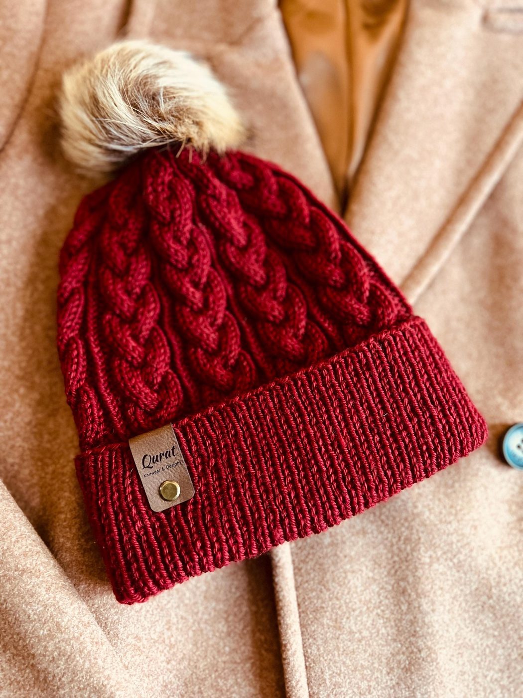 Deep red hand-knit cable toque with a faux-fur pom and Qurat leather tag